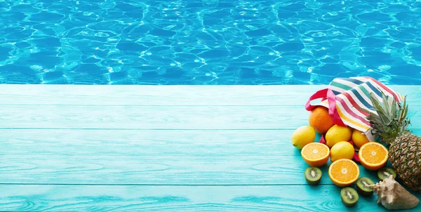 Summer holiday banner background. Fruits on blue wooden floor near swimming pool. Oranges, pineapple, kiwi, lemon food. Sea shell. Selective focus. Copy space. Beach concept
