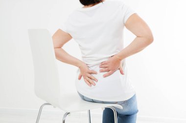 Sandalyede oturan orta yaşlı esmer kadın sırt ağrısı çekiyor, ilaç kullanıyor.