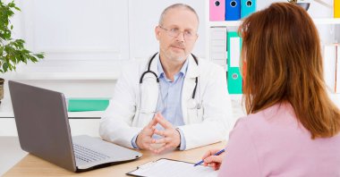 Masadaki erkek doktor hastayla iletişim kuruyor.
