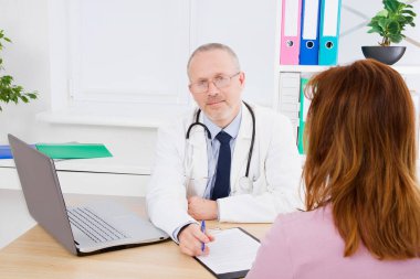 Doktor kadın hastayla konuşuyor ve sağlık ofisinde oturuyor. Beyaz üniformalı bir adam. Sağlık sigortası. Uzayı kopyala Kaliteli tıp konsepti.