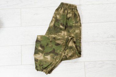 Closeup Camouflage pants on wooden background, green khaki pants. Unfolded camouflage soldier elastic pants on wooden background. clipart