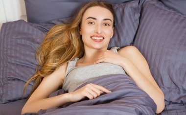 Kapat. Mutlu genç kadın sabah yatakta uyanıyor.