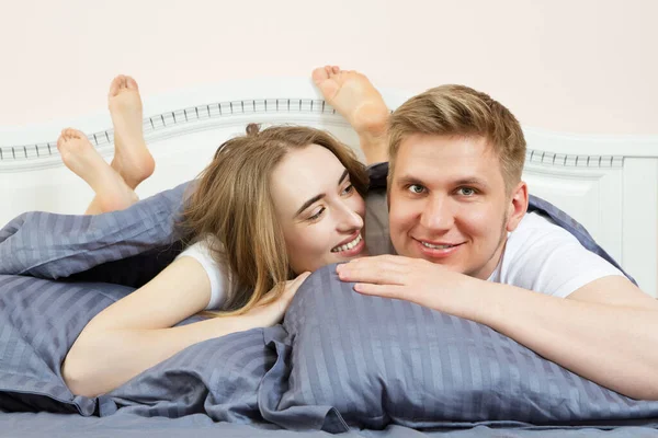 Cute loving couple is lying on the bed in the bedroom in the morning. Young happy couple lying in bed and smile
