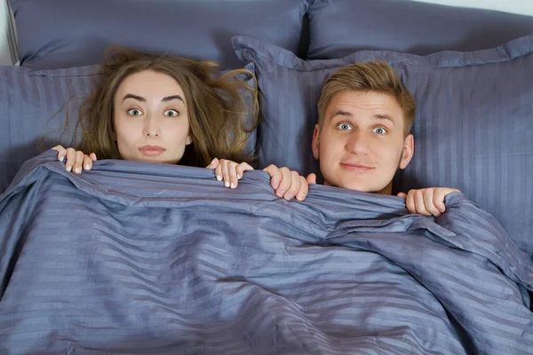 A guy and a girl hide their faces behind a blanket, a happy couple in bed