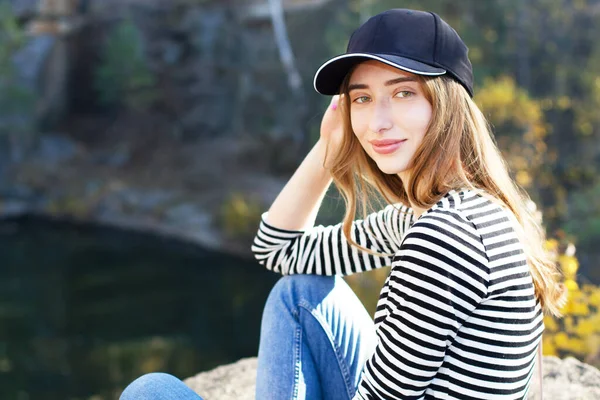 Beautiful young active woman on a background of a beautiful view of the forest and rocks. Girl wearing a cap and casual clothes - active life concept