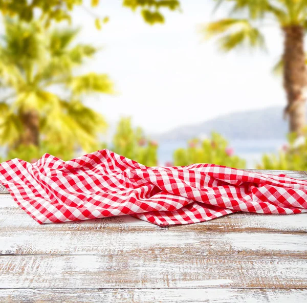 checkered tablecloth on old wooden table on blurred park background, holiday concept