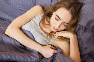 Yatakta uyuyan bir kadın, bir yastığın üzerinde elleri başının yanında dinlenen bir kadın. Ve omzunu örten bir yorgan..