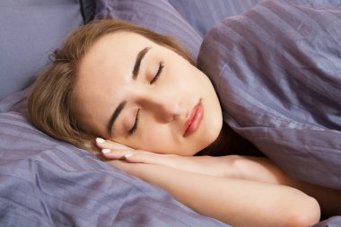 Evdeki yatakta uyuyan genç bir kadının portresi. Yakın plan.