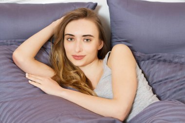 İyi sabahlar. Pozitif güzel bir kadın kameraya gülümsüyor, iyi bir uykudan sonra yatakta yatıyor.