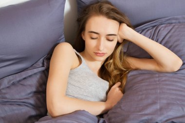 Genç ve güzel bir kadın sabahları yatakta güneşleniyor. Güzel manken yüzü kamerada seksi görünüyor, kız yatak odasında uyuyor.