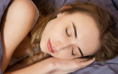 Yatakta rahat ve mutlu bir şekilde uzanırken uyuyan güzel genç bir kadının portresi. Yüzündeki pencereden güneş parlıyor.