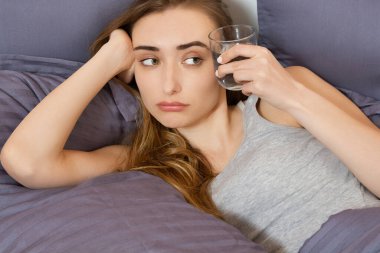 Kadın akşamdan kalma, kadın yatağa uzanmış bir bardak su tutuyor. Başı ağrıyan bir kız. Genç bir kadın sabah hasta olur, baş ağrısı ya da hamilelik zehirlenmesi.