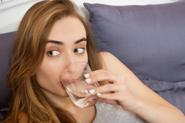 Kadın akşamdan kalma, kadın yatağa uzanmış bir bardak su tutuyor. Başı ağrıyan bir kız. Genç bir kadın sabah hasta olur, baş ağrısı ya da hamilelik zehirlenmesi.