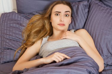 Uykusuzluk çeken ya da evde yatağında rahatsız olan ve kameraya bakan bir kadın.