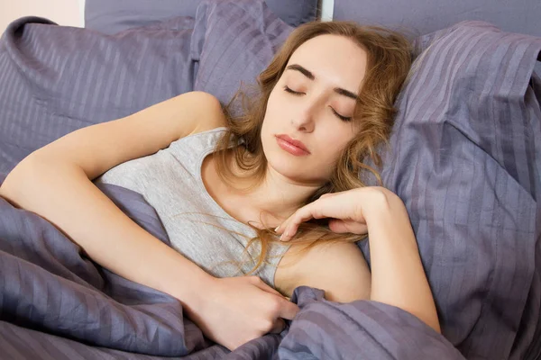 Güzel genç bir kadın sabahları yatakta güneşleniyor. Güzel manken yüzü kamerada seksi görünüyor, kız yatak odasında uyuyor.