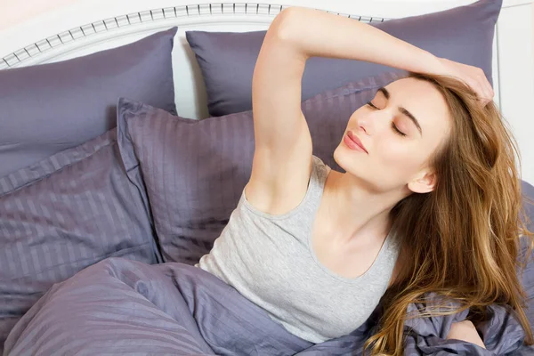 Sabahleyin modern bir dairede yatağında güzel beyaz bir kızın portresi. Gözlerini kapalı tutuyor ve tatmin olmuş görünüyor. Güzel genç bir kadın sabahları yatakta güneşleniyor. Güzel Model yüzü