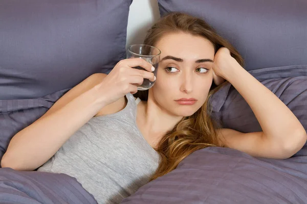 Feeling bad from a hangover in the morning : young woman hold glass of water and lying in bed bedroom