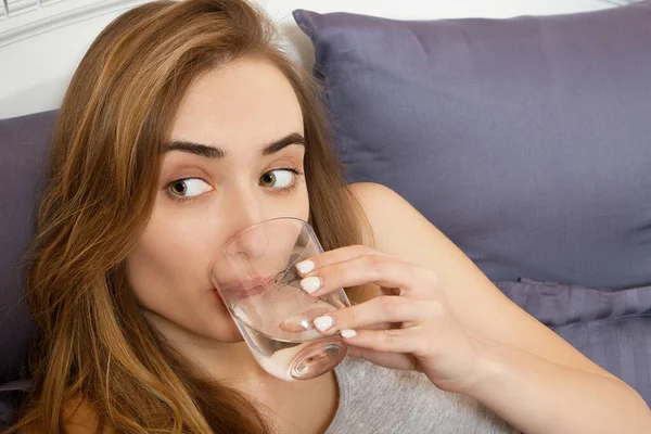 Kadın akşamdan kalma, kadın yatağa uzanmış bir bardak su tutuyor. Başı ağrıyan bir kız. Genç bir kadın sabah hasta olur, baş ağrısı ya da hamilelik zehirlenmesi.