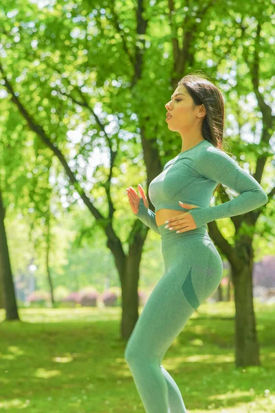 Şehir parkındaki egzersiz sırasında koşan ve zıplayan zeytin yeşili spor kıyafetli çekici bir esmer kız.