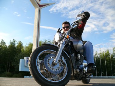 Classical biker Klimenko Oleg in black spectacles sits on chopper. Nadym, Russia. clipart