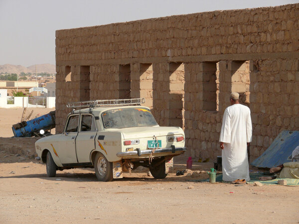 Soviet car Moskvich 412 closeup in Wadi - Halfa, Sudan - November 19, 2008. Unknown man near the car. Architectural building.