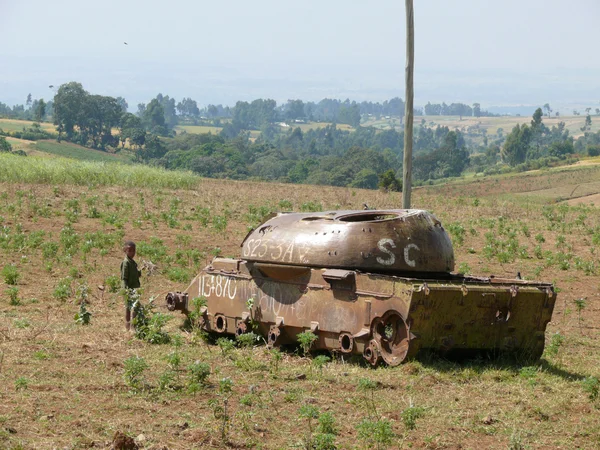 JIGA, ETIOPÍA - 24 DE NOVIEMBRE DE 2008: Tanque soviético en los viejos tiempos. Un niño desconocido parado cerca del tanque. Paisaje natural, vegetación en el valle . —  Fotos de Stock