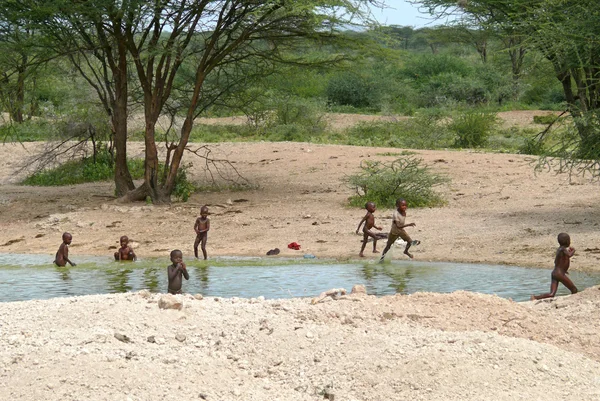 Isiolo, kenya - 28 november 2008: okända kenyanska barn badar i floden i isiolo, kenya - 28 november 2008. floden och träd runt. — Stockfoto