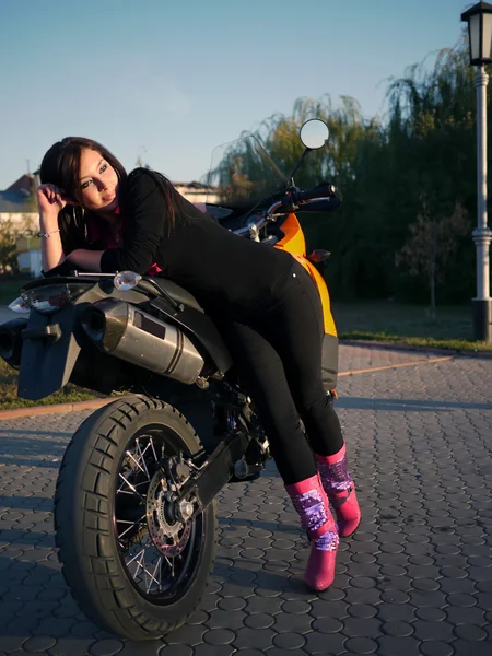 Vacker ung brunett på bakgrund av en motorcykel i th — Stockfoto