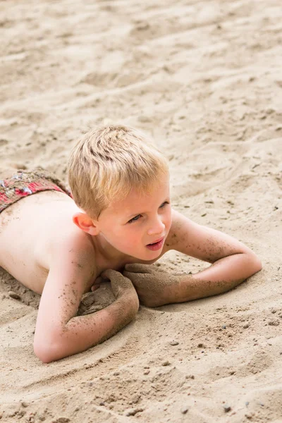 Jeune garçon allongé sur une plage de sable — Photo