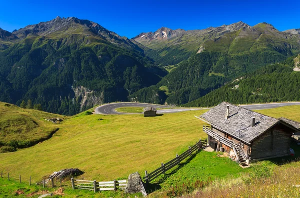 Alpine road with mountain hut in the foreground — Stock Photo, Image