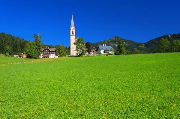 Zelená louka v alpské vesnice s kostelem v dálce — Stock fotografie