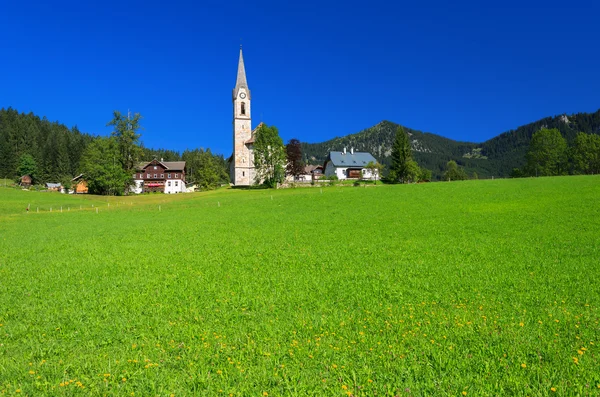 Grüne Wiese im Alpendorf mit Kirche in der Ferne — Stockfoto