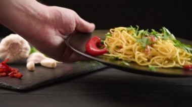 Bir adam masaya bir tabak makarna koyar. Koyu arkaplanda geleneksel İtalyan makarnası