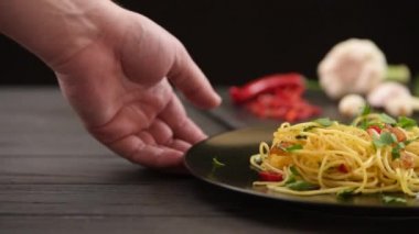Bir adam masaya bir tabak makarna koyar ve sonra makarnayı alır. Koyu arkaplanda geleneksel İtalyan makarnası