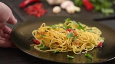 Bir adam masaya bir tabak makarna koyar ve sonra makarnayı alır. Koyu arkaplanda geleneksel İtalyan makarnası.