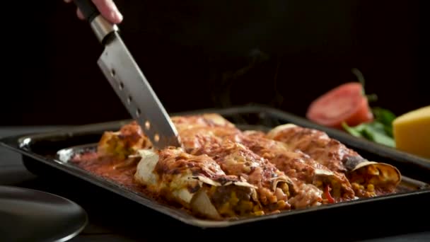 Cooked enchiladas are sliced to serve on a dark background — Stockvideo