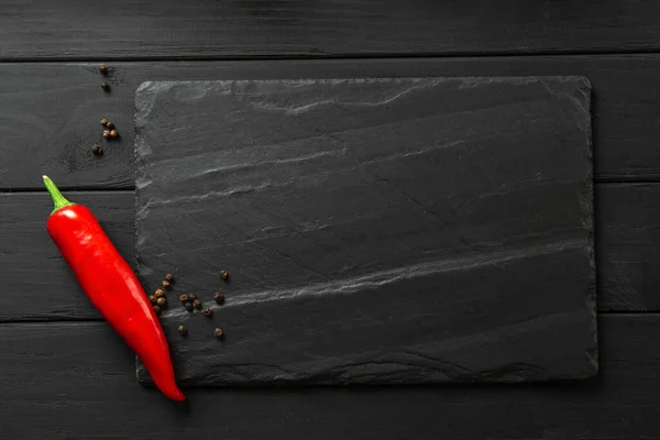 Square slate board in dark color. chili peppers and spices on black background layout with space for text, top view — Stockfoto