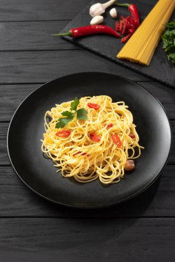 Pasta Aglio, Olio e Peperoncino, İtalyan spagettisi sarımsaklı, acı biberli ve zeytinyağlı, beton bir masada siyah bir tabakta, yukarıdan dikey manzaralı, geleneksel bir İtalyan yemeği. Makarna devam