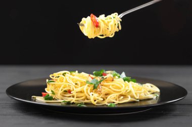 İtalyan makarna çatalı. Siyah arka planda spagetti olan tabak. Yanında makarna yapmak için malzemeler var..