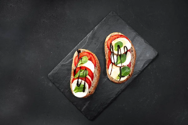 Open sandwiches, with an open sliced sourdough bread sandwich with cherry tomatoes, mini mozzarella, fresh basil, olive oil and oregano in the center of the board. Top view