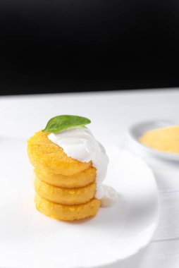 Ekşi kremayla kızartılmış krep. Arka planda hafif bir tabakta. Kavram. Makarna peyniriyle karartılmış arka planda kızarmış polenta. Yan görüş. Dikey çekim