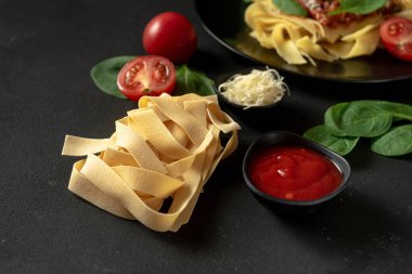 Koyu arkaplanlı, içinde yemek pişirmek için malzemeler olan hamur hamurlu makarna. Makarna pappardelle bolonez sosuyla hazırlanır. Klasik İtalyan tarifi.