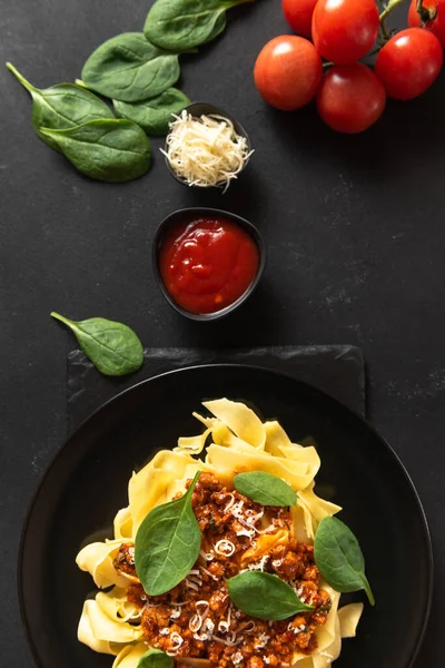 Classic food in Italy. Pasta with bolognese sauce on a black plate with cheese and basil. Top view and vertical frame