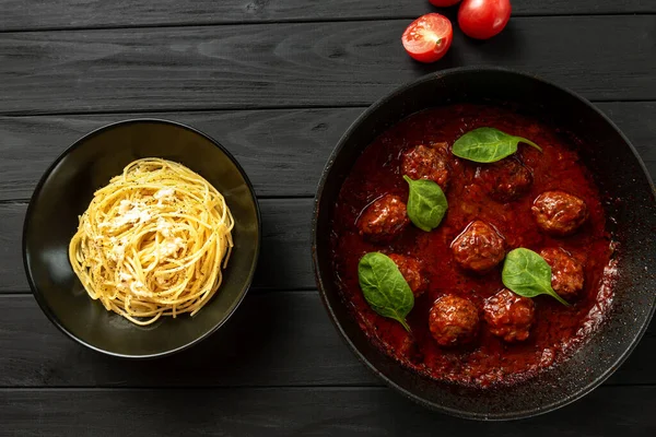 The process of making Italian pasta with meat balls. A plate of spaghetti stands apart from the meatballs on a griddle on a dark background.