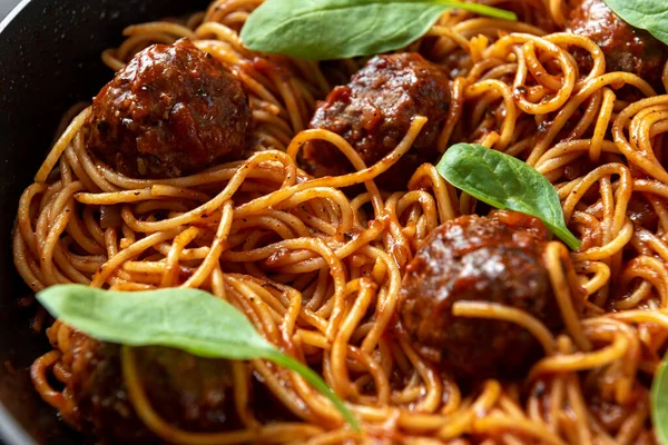 The process of making Italian pasta with meat balls. A plate of spaghetti stands apart from the meatballs on a griddle on a dark background. Close up