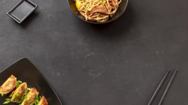 Asya yemekleri, gyozo ve udon eriştesi. Karanlık bir arka planda pişirilmiş Japon yemeklerini canlandırmak. Soya soslu gyozo ve udon eriştesi pişirdim. Asya yemeklerinin hareketli animasyonunu durdurun. Vejetaryen