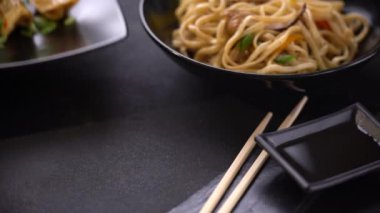 Tabakta Japon gyozo köftesi var. Kızarmış hamur köfteleri ve udon eriştelerinden oluşan karanlık bir arka planda Asya yemeği. Kızarmış ve udon eriştelerinin koyu arka planında Asya yemekleri. - Evet. Vejetaryen Asyalı