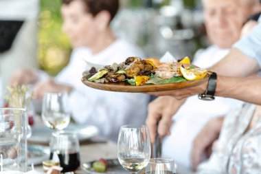 Garson restoran misafirlerine servis yapıyor. Garson elinde karides ve sebzeli bir tepsi tutuyor..