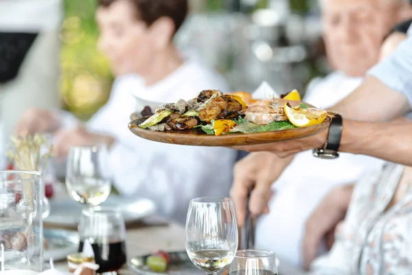 Garson restoran misafirlerine servis yapıyor. Garson elinde karides ve sebzeli bir tepsi tutuyor..