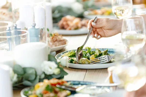 Kaşıklı bir kadın eli salatayı alır. Restoran atmosferi. Hazır yemekler masanın üzerinde. İnsanlar restoranda yemek yer.